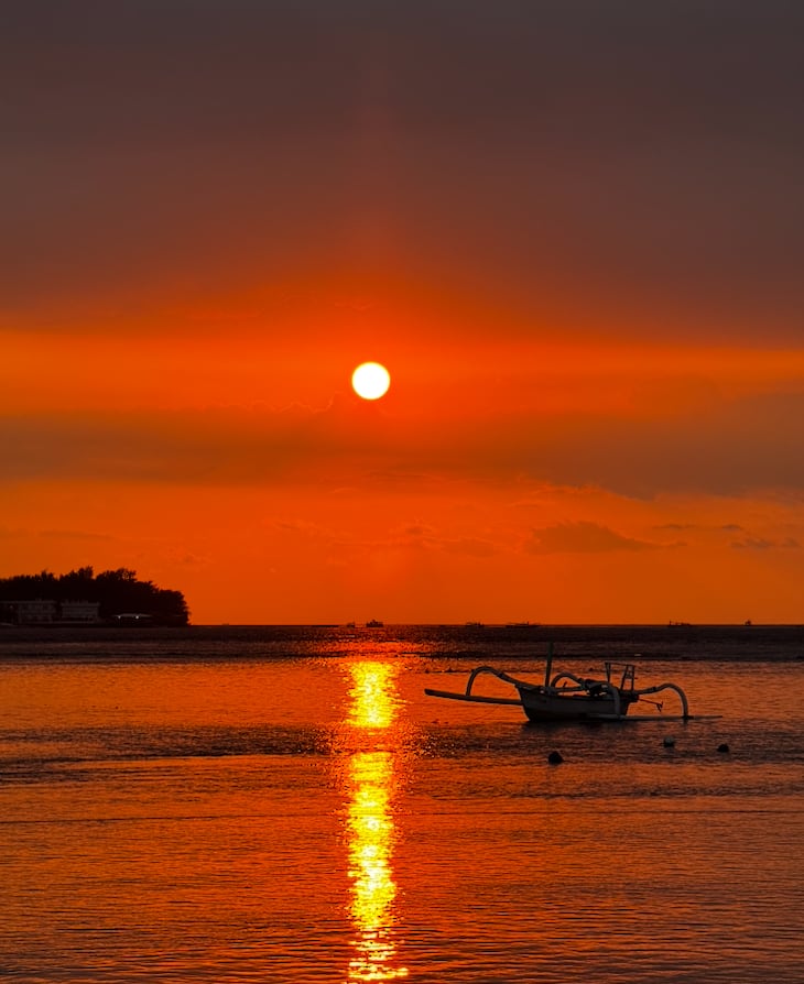 World-class sunset over the ocean at Gili Meno with a traditional outrigger boat